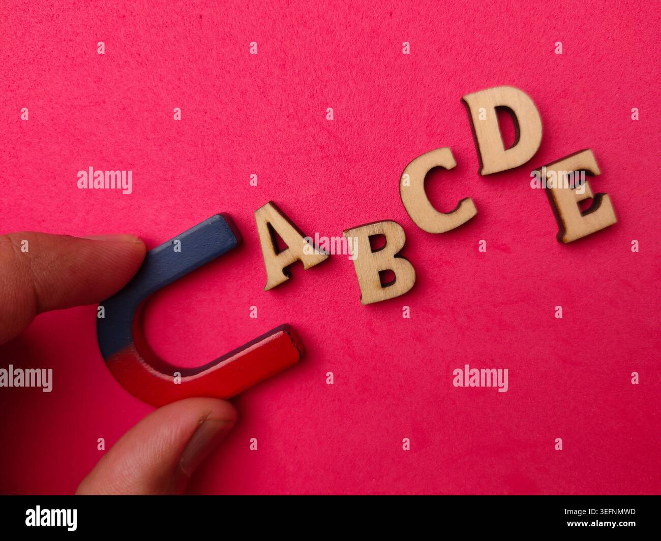 La mano tiene un magnete vicino alle lettere alfabetiche in legno A B C D e disposte su uno sfondo rosa. Foto Stock