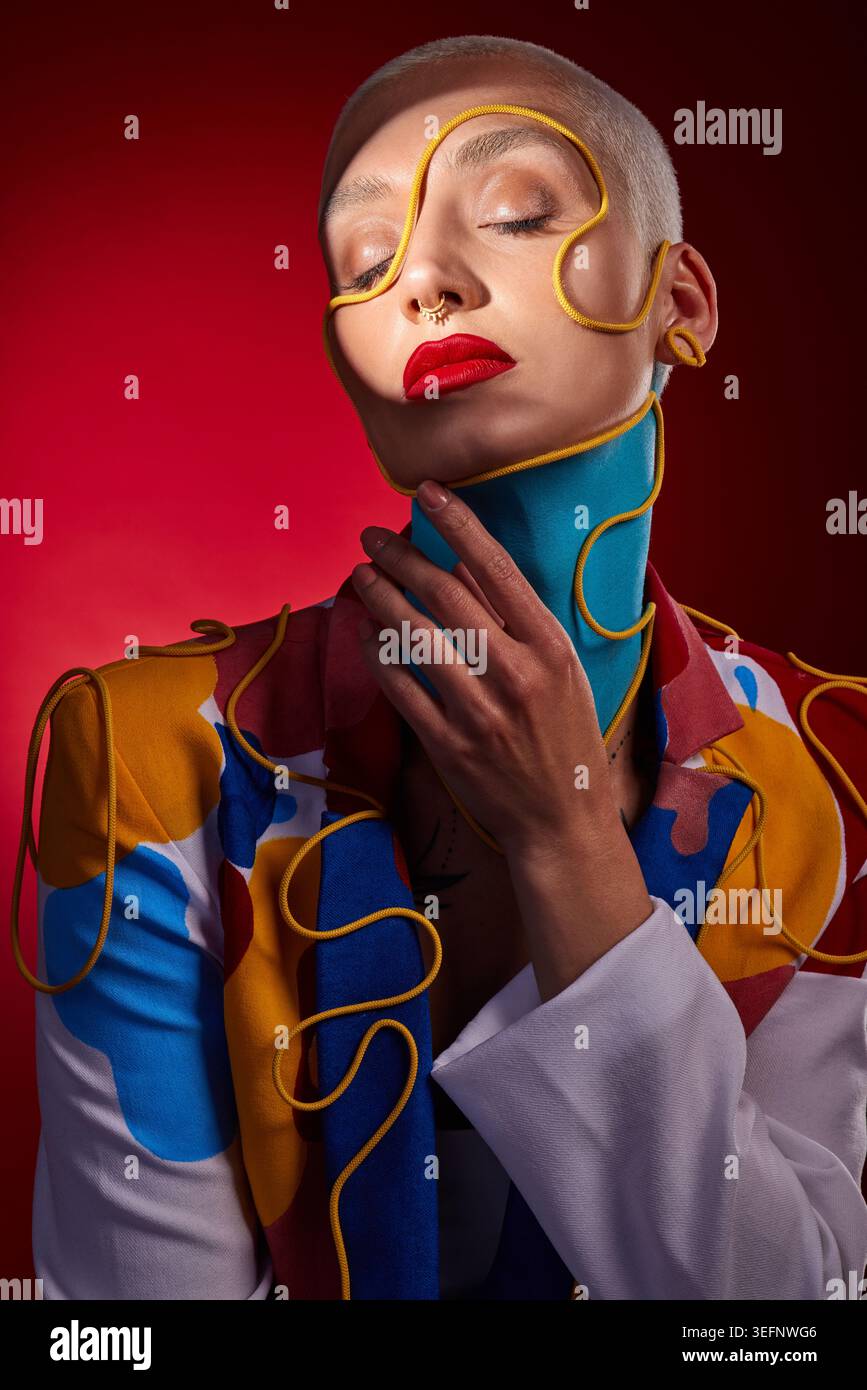Moda, creativa e donna con gli occhi chiusi in studio per un'arte o uno stile unici su sfondo rosso. Persona diversa, alla moda e femminile in stilista Foto Stock