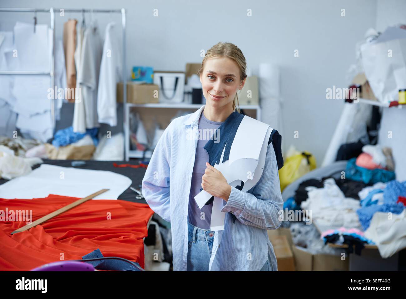 Creatrice femminile in uno studio ingombrante che presenta campioni di moda sostenibili Foto Stock
