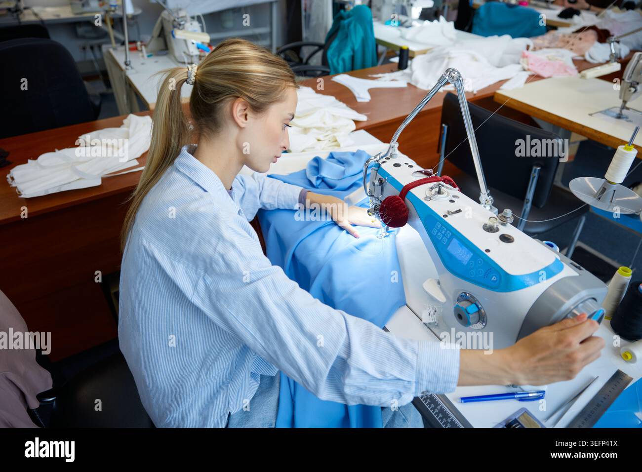 Sarta che gestisce in modo esperto il tessuto attraverso il processo di cucito industriale Foto Stock