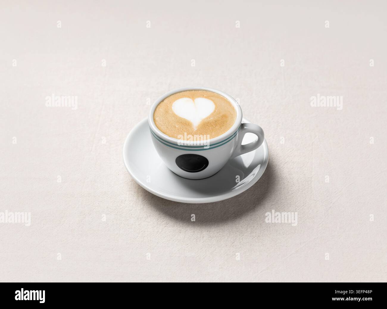 Un cappuccino con crema di latte decorato con latte art a cuore servito in una tazza bianca su un piattino. Le tonalità calde e la luce soffusa lo rendono ideale per un caffè Foto Stock