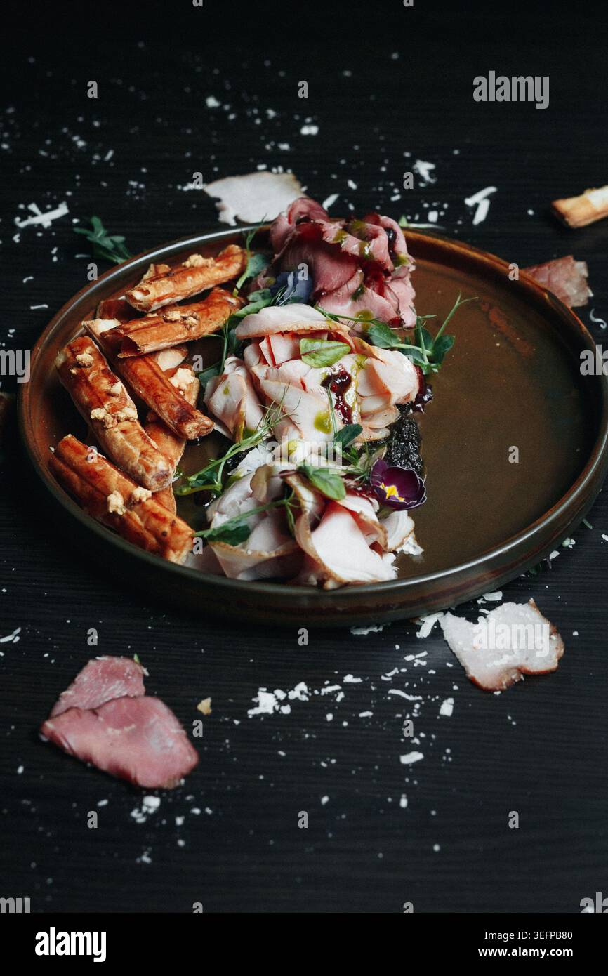 Piatto gourmet placcato con carne, erbe e formaggio su superficie rustica Foto Stock