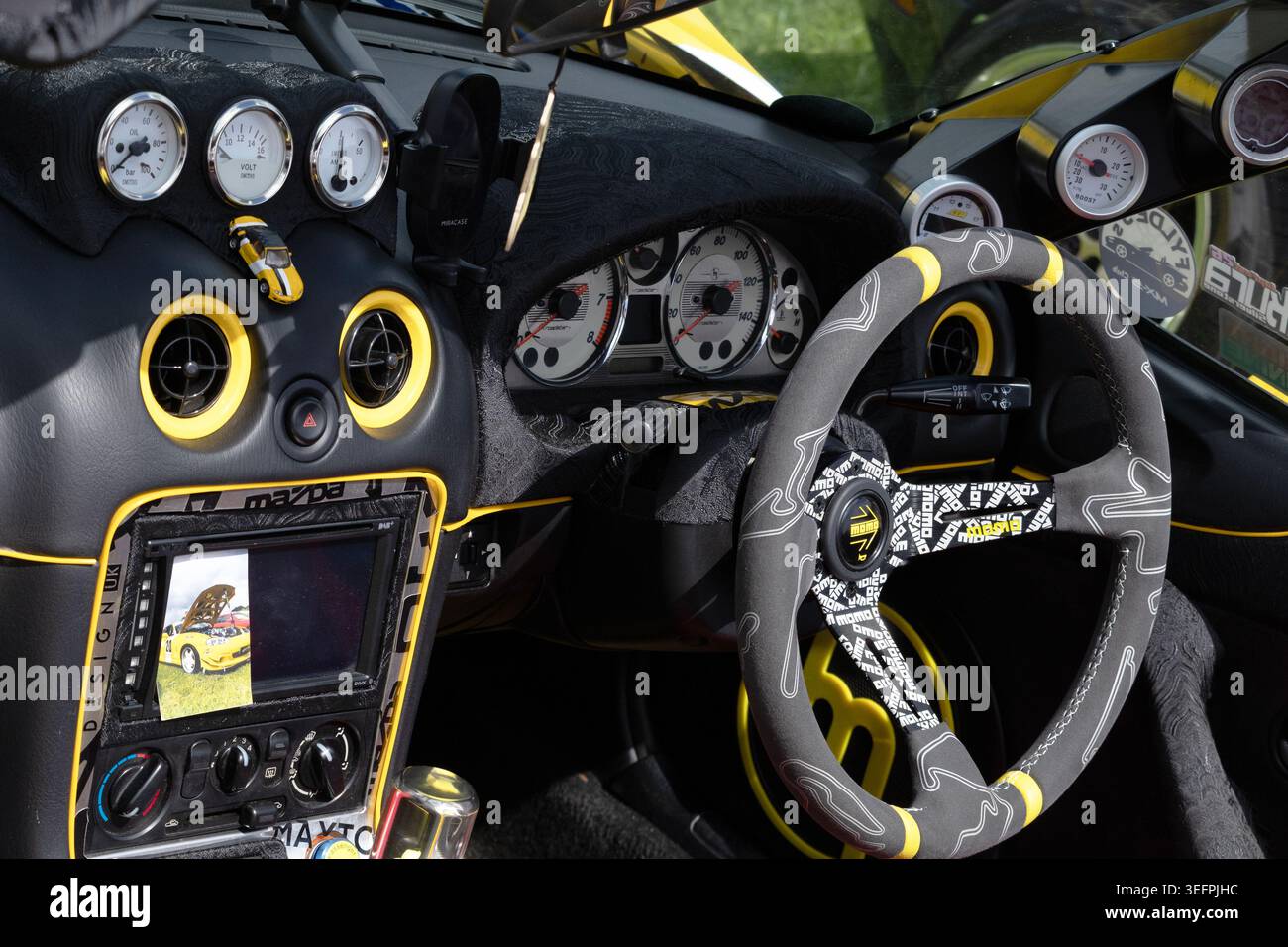 Una ripresa dell'interno di una Mazda MX-5 Miata (NB) con guida a destra personalizzata mostra un design nero e giallo sorprendente con un volante Momo. Foto Stock