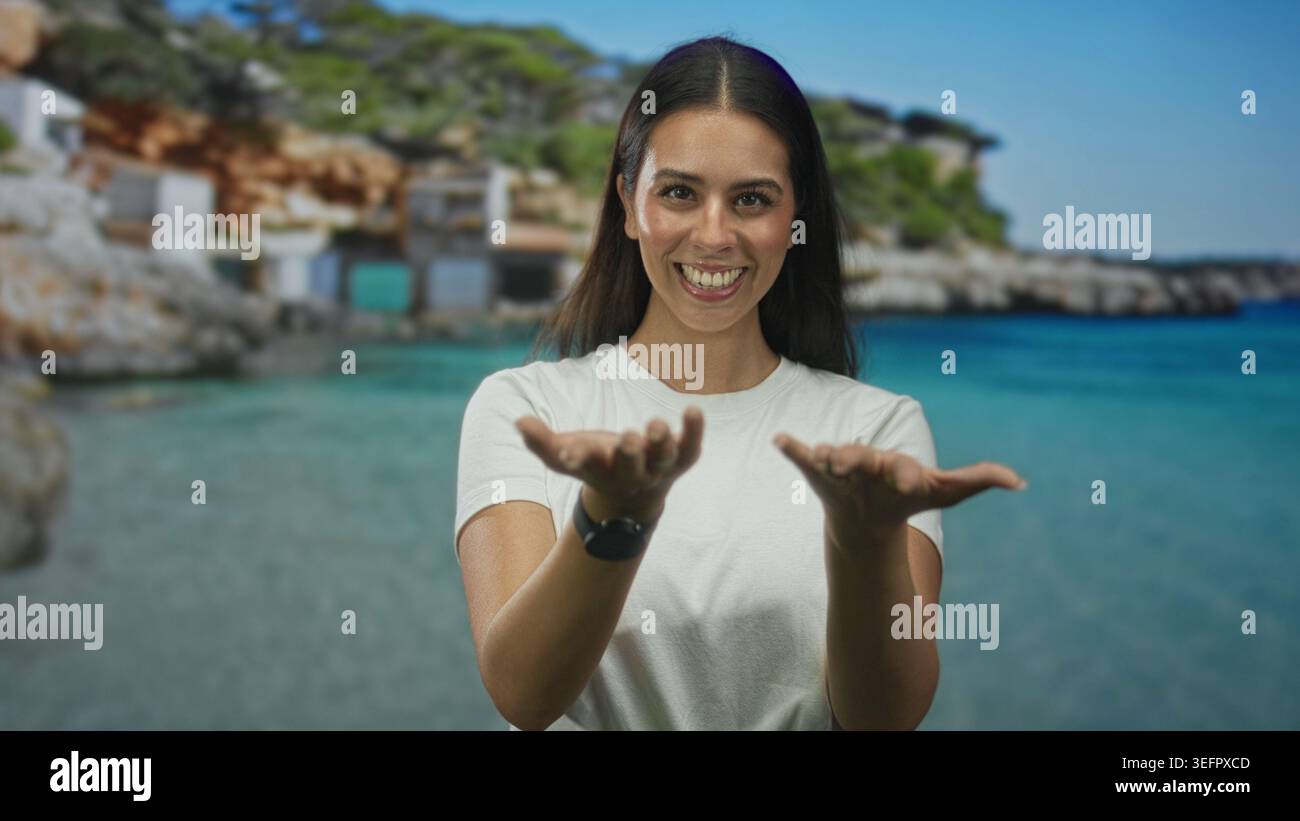 Donna sorridente con le mani aperte che mostra le palme e guarda in un set da studio sul mare; gioia per i viaggi estivi. Foto Stock