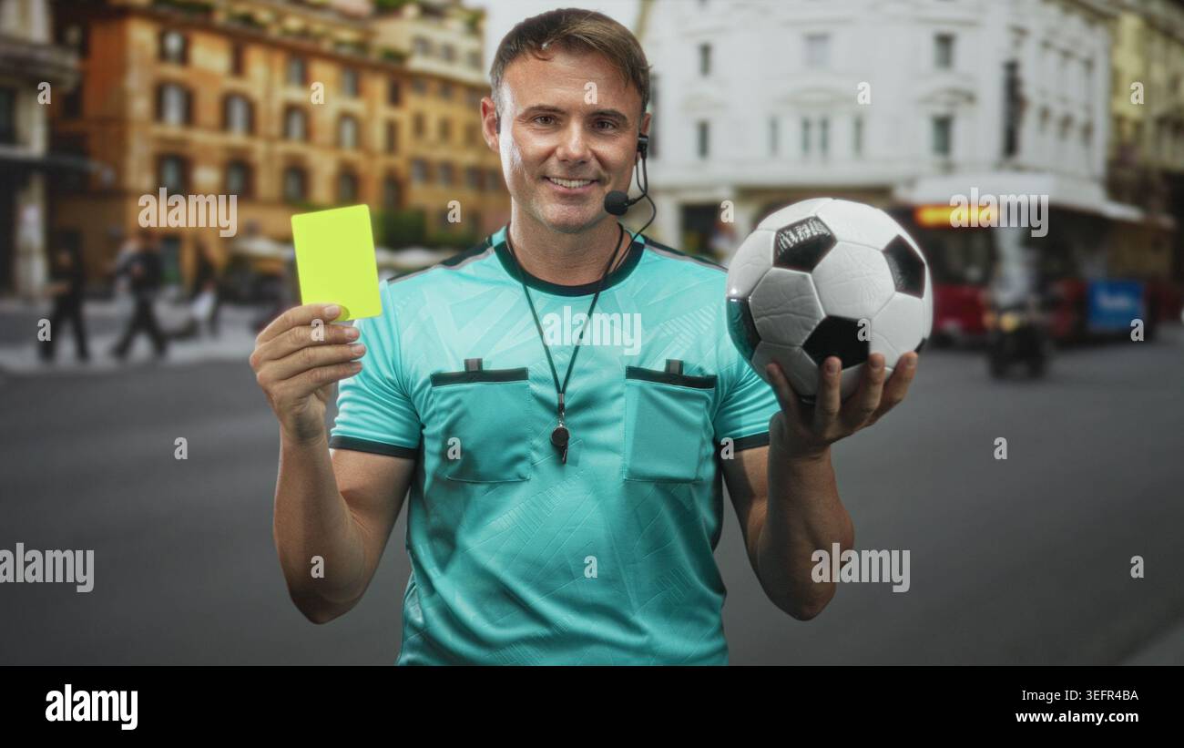 L'arbitro uomo tiene la carta gialla e la palla da calcio in strada, indossando fischio e cuffie; sicurezza nel fair play. Foto Stock
