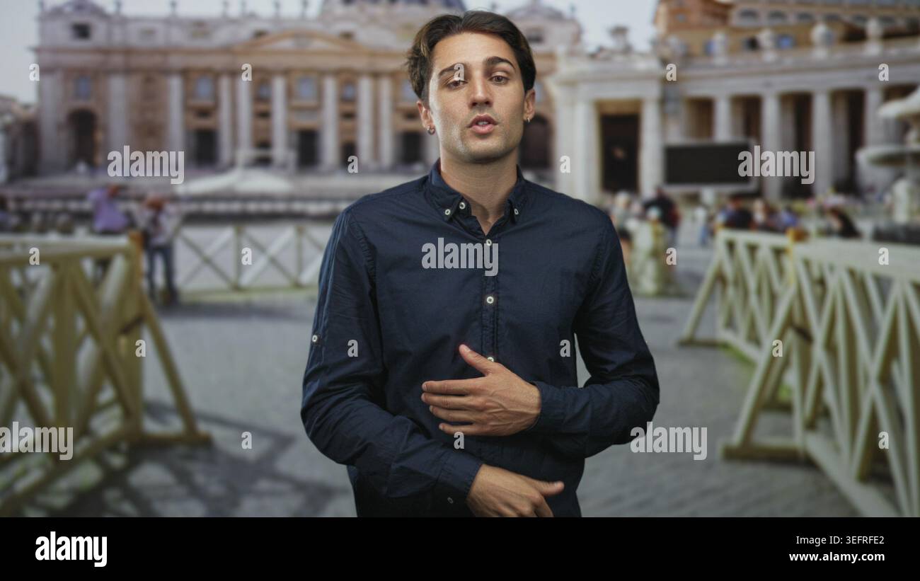 Il giovane punta il dito e mette la mano sul petto mentre parla di fronte a un edificio storico della basilica con folla e barriere; viaggia con informazioni. Foto Stock