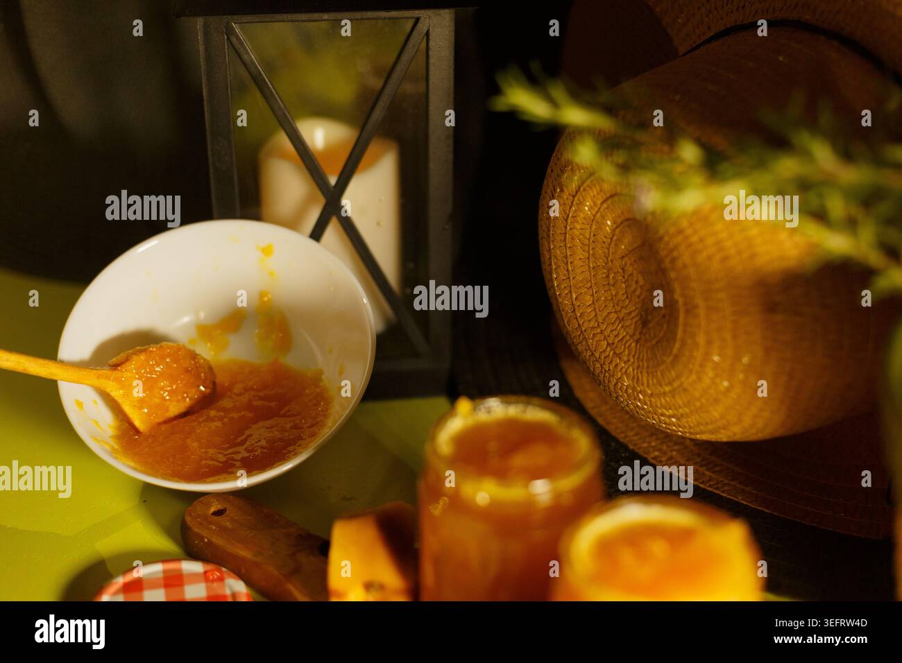 Vasetti con marmellata rustica illuminata dal sole e ciotola sul tavolo di legno, marmellata d'oro con cucchiaio, barattolo Mason con scacchi Foto Stock