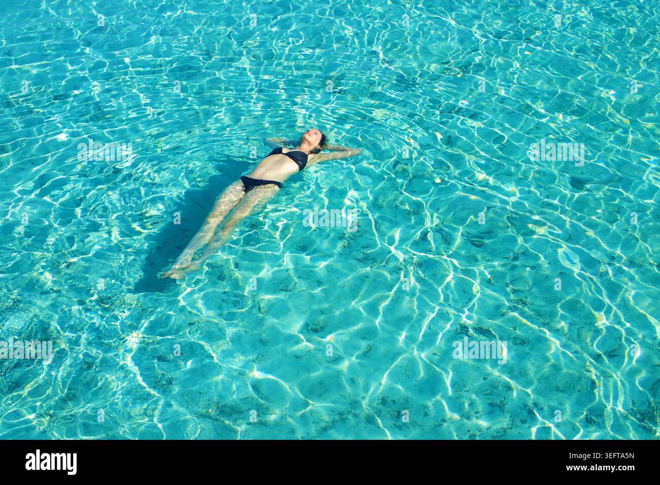 Donna in bikini che si rilassa e galleggia sulla schiena nelle splendide acque turchesi delle Maldive Foto Stock