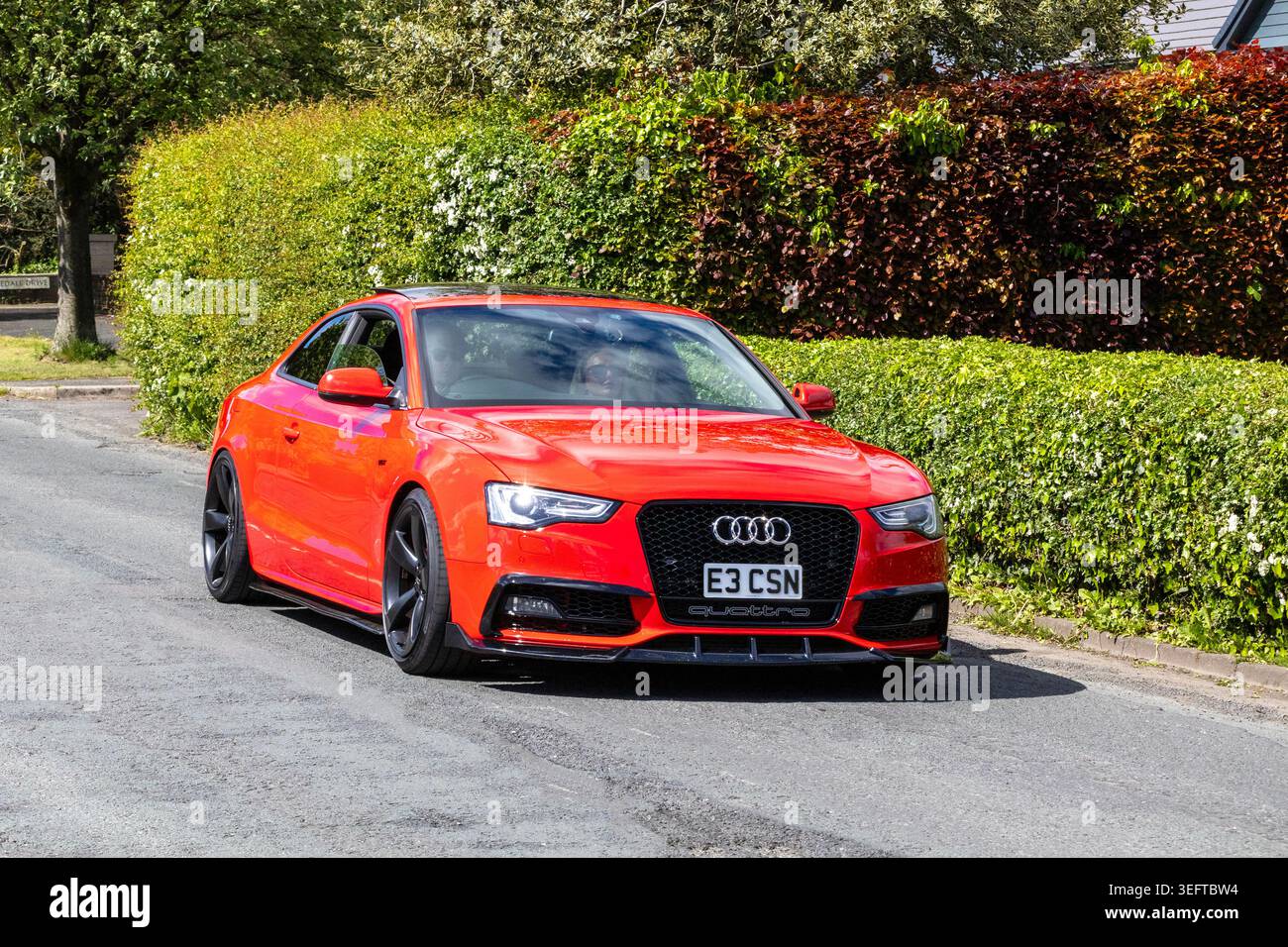 Una coupé Audi S5 rosso brillante modificata con griglia nera a nido d'ape, sospensioni abbassate e splitter anteriore personalizzato che passa sulla strada. Foto Stock