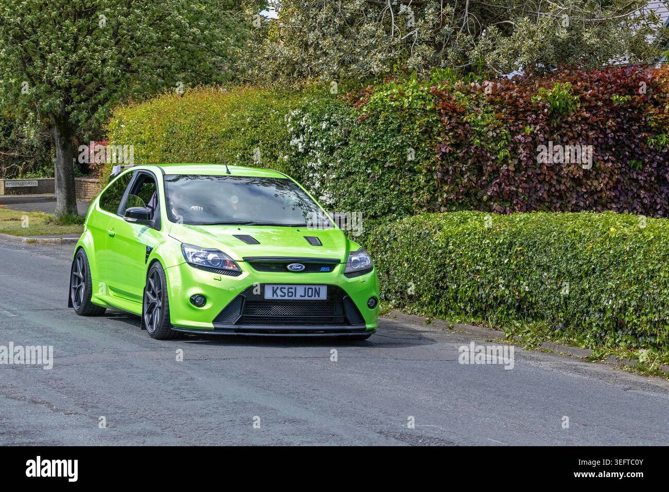 Una vivace hatchback sportiva Ford Focus RS Mk2 verde ultimate che passa davanti a siepi rigogliose in una tranquilla strada residenziale. Foto Stock