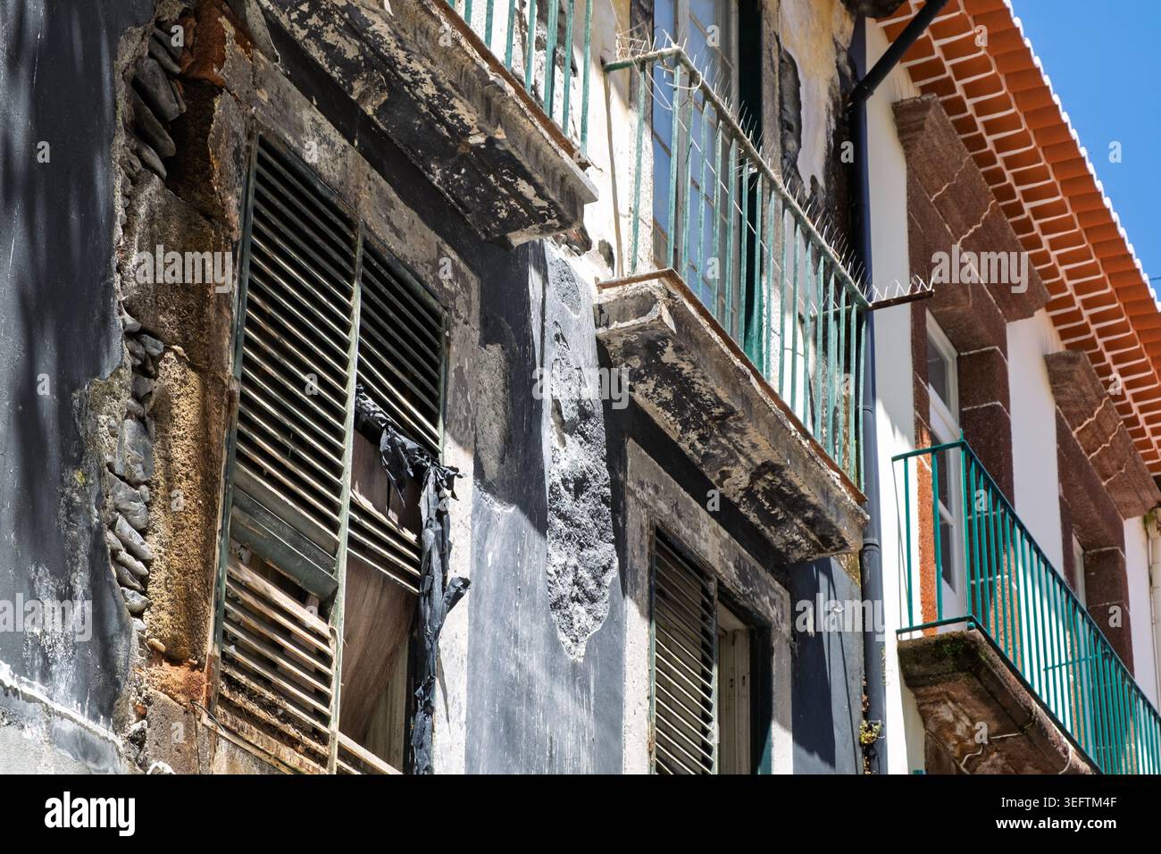 Funchal, Madeira, 11 maggio 2026. Edificio facciate sotto un cielo blu. Un edificio presenta pietra esposta con vernice scura e persiane danneggiate. Foto Stock