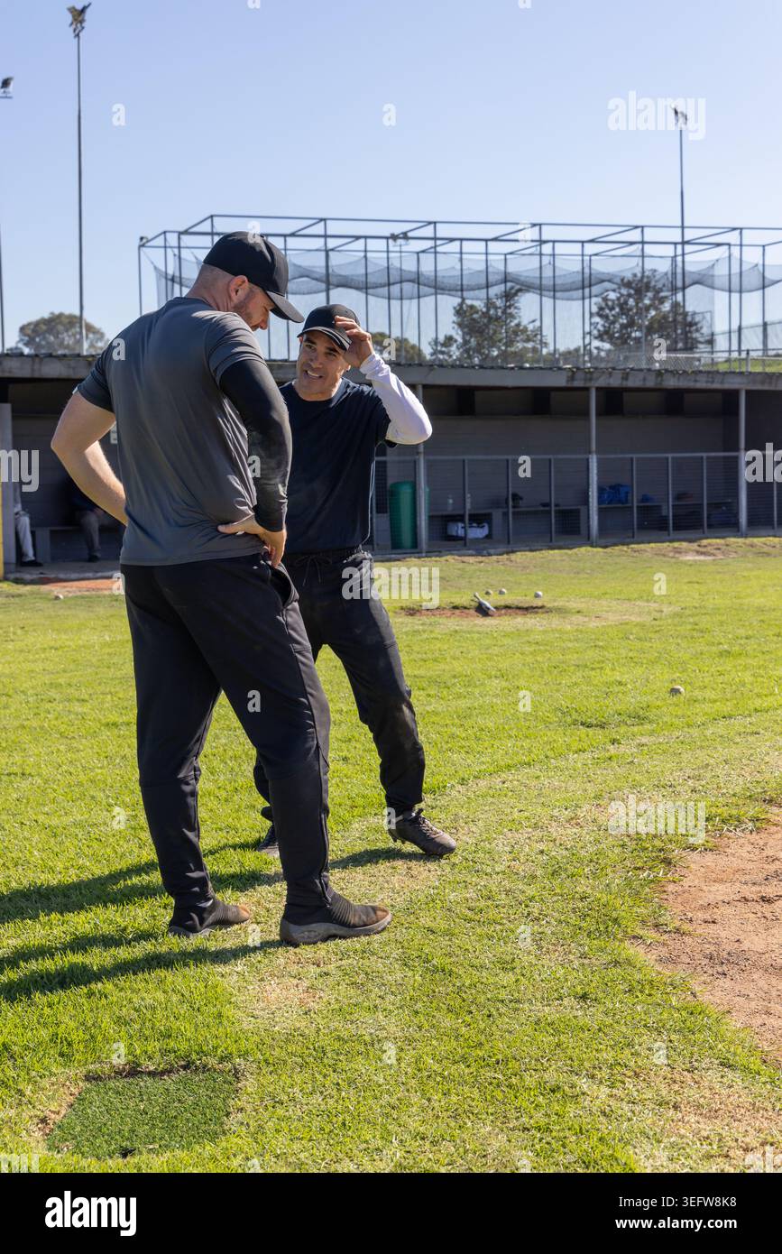 Due uomini, uno anziano, in piedi sul campo di allenamento di baseball vicino al dugout, un cappello di regolazione Foto Stock
