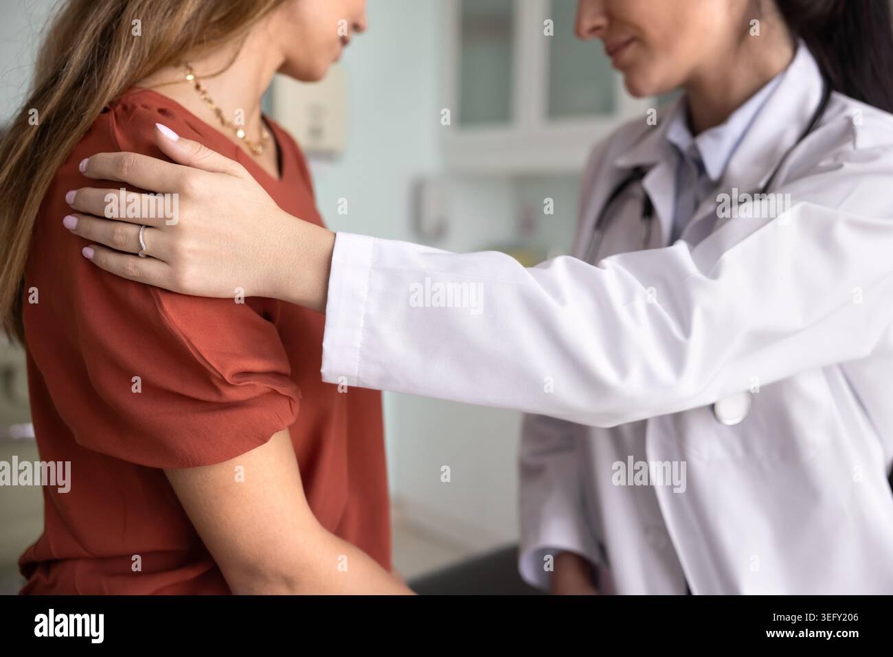 Medico che pone delicatamente la mano sulla spalla della paziente, primo piano Foto Stock