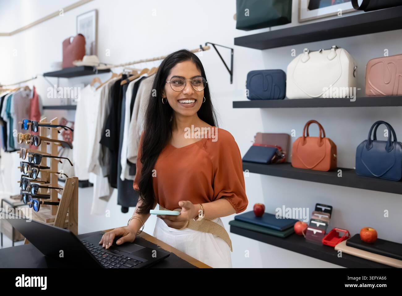 L'assistente del negozio con telefono e laptop si trova al banco cassa Foto Stock