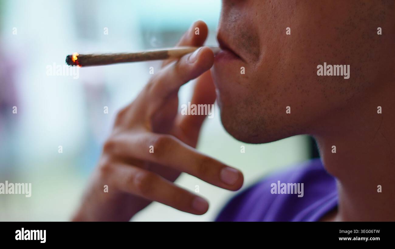 Persona che espone fumo da un'articolazione di marijuana illuminata, che consuma cannabis Foto Stock