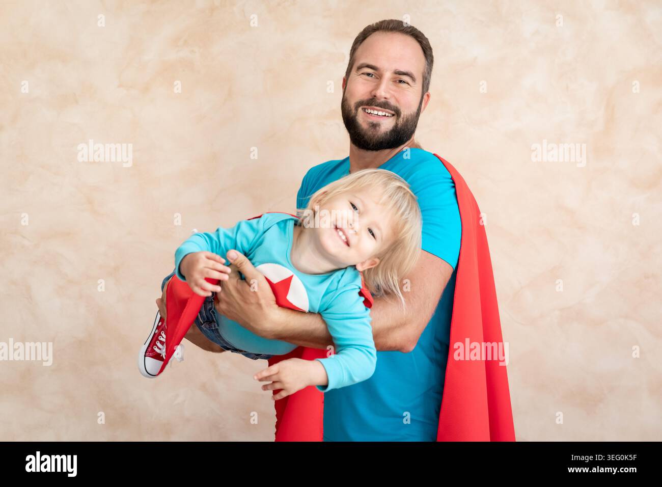 Un uomo e un bambino super eroe a casa. Padre e figlio supereroi che si divertono insieme. Concetto di vacanza in famiglia. Felice giornata di papà Foto Stock