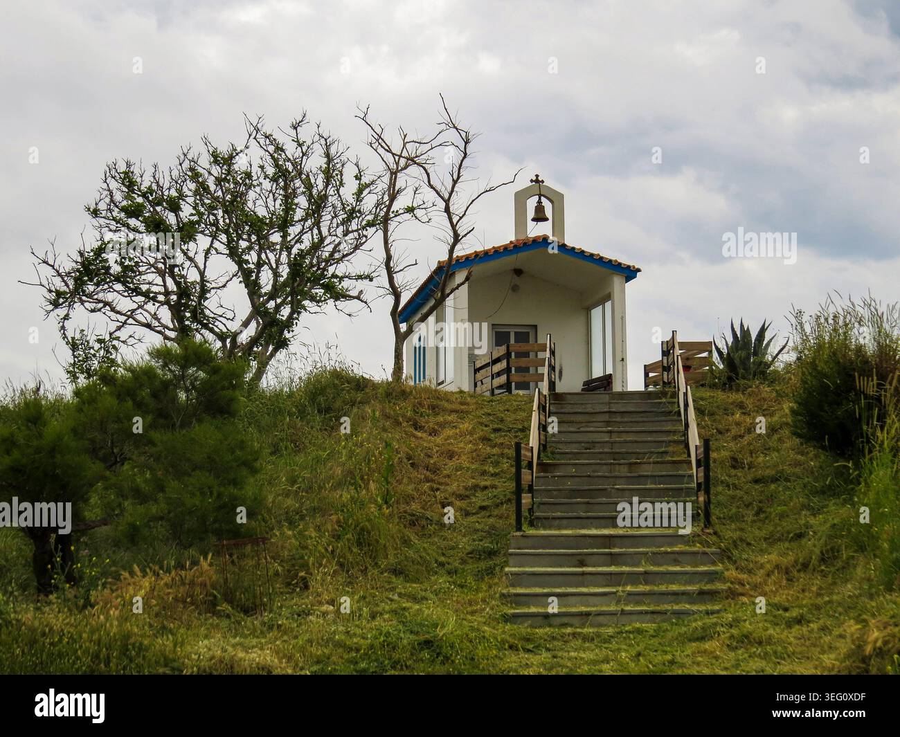 Piccola chiesa bianca tradizionale con una campana su una collina erbosa sotto il cielo nuvoloso. Foto Stock