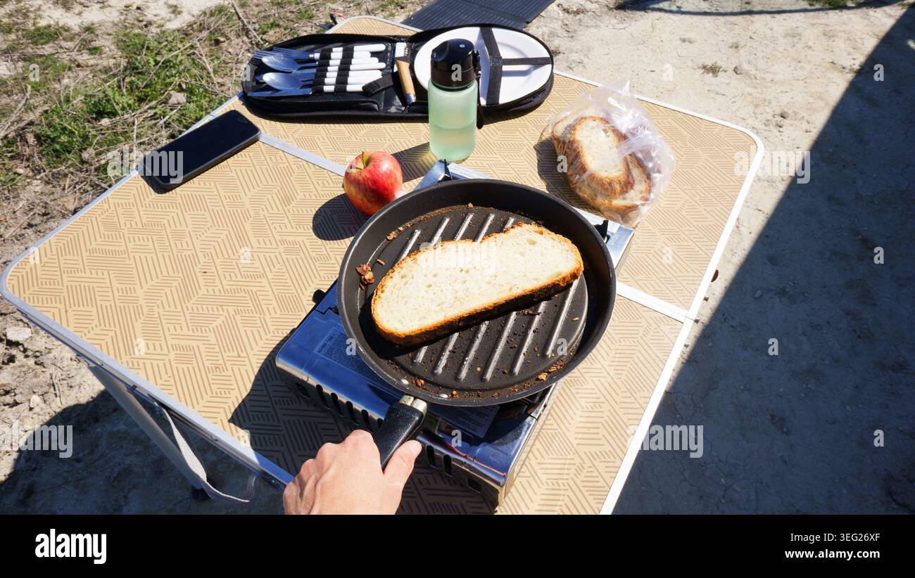 Persona che tosta il pane su una stufa a gas portatile durante una colazione all'aperto Foto Stock