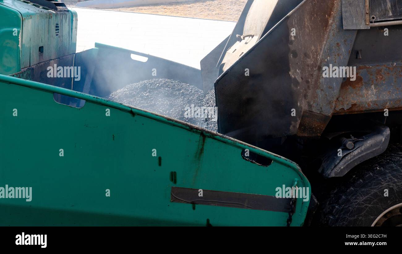Primo piano di macchine per pavimentazione dell'asfalto in azione, caricando asfalto fresco sulla strada. L'attrezzatura viene utilizzata per pavimentazioni stradali efficienti e per la ripavimentazione stradale Foto Stock