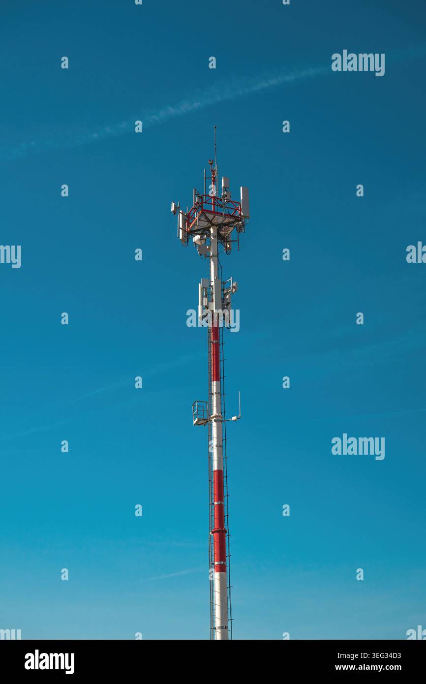 Torre di celle rosse e bianche con antenne contro il cielo azzurro per telecomunicazioni e connettività, immagine verticale. Foto Stock