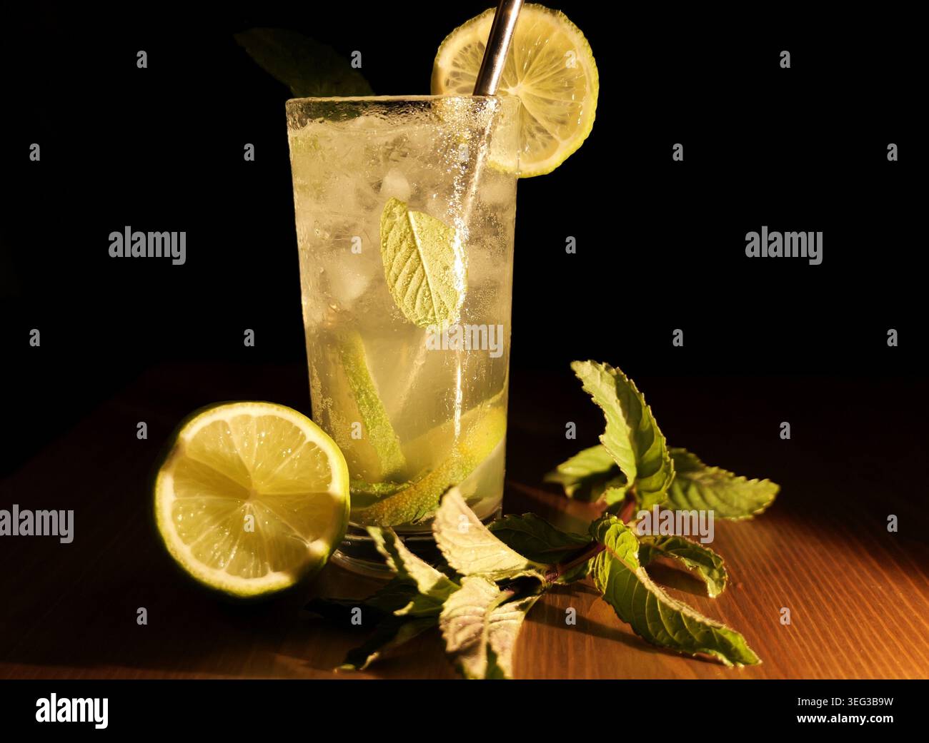 Rinfrescante mojito in un alto bicchiere con fetta di lime, menta fresca e ghiaccio, bibita frizzante su un tavolo di legno su sfondo scuro per un'atmosfera fresca e tropica Foto Stock