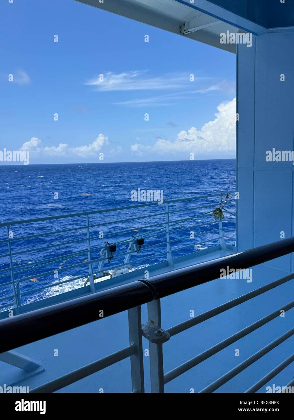 Vista panoramica delle profonde onde blu dell'oceano e di un cielo luminoso con nuvole bianche chiare, incorniciate dalle ringhiere metalliche di un ponte delle navi da crociera. - Immagine stock catturata con smartphone