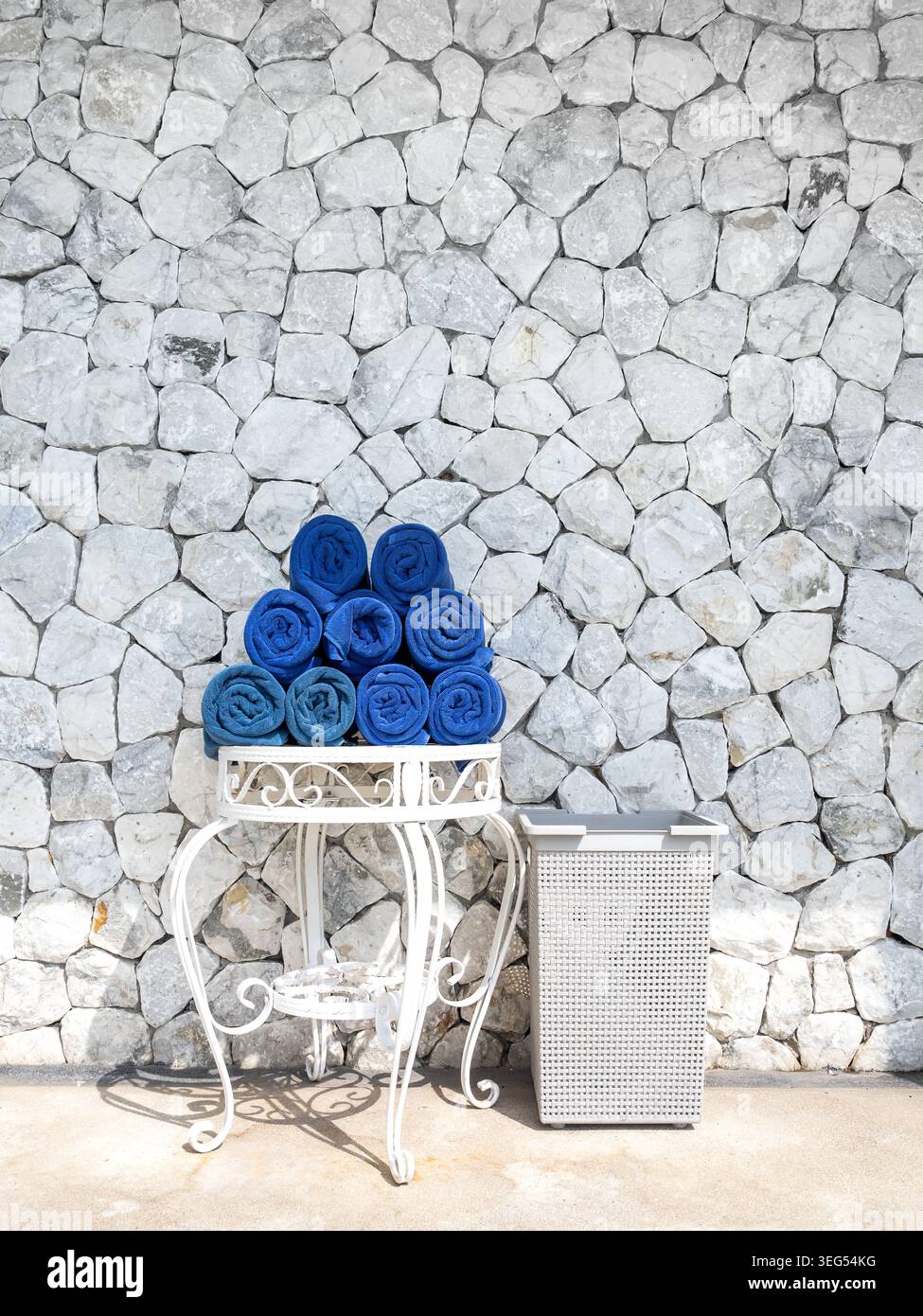 Una pila di asciugamani blu preparati per gli ospiti dell'hotel presso la piscina con pareti in pietra, concetto di servizio di ospitalità pulito, servizi di lusso del resort Foto Stock
