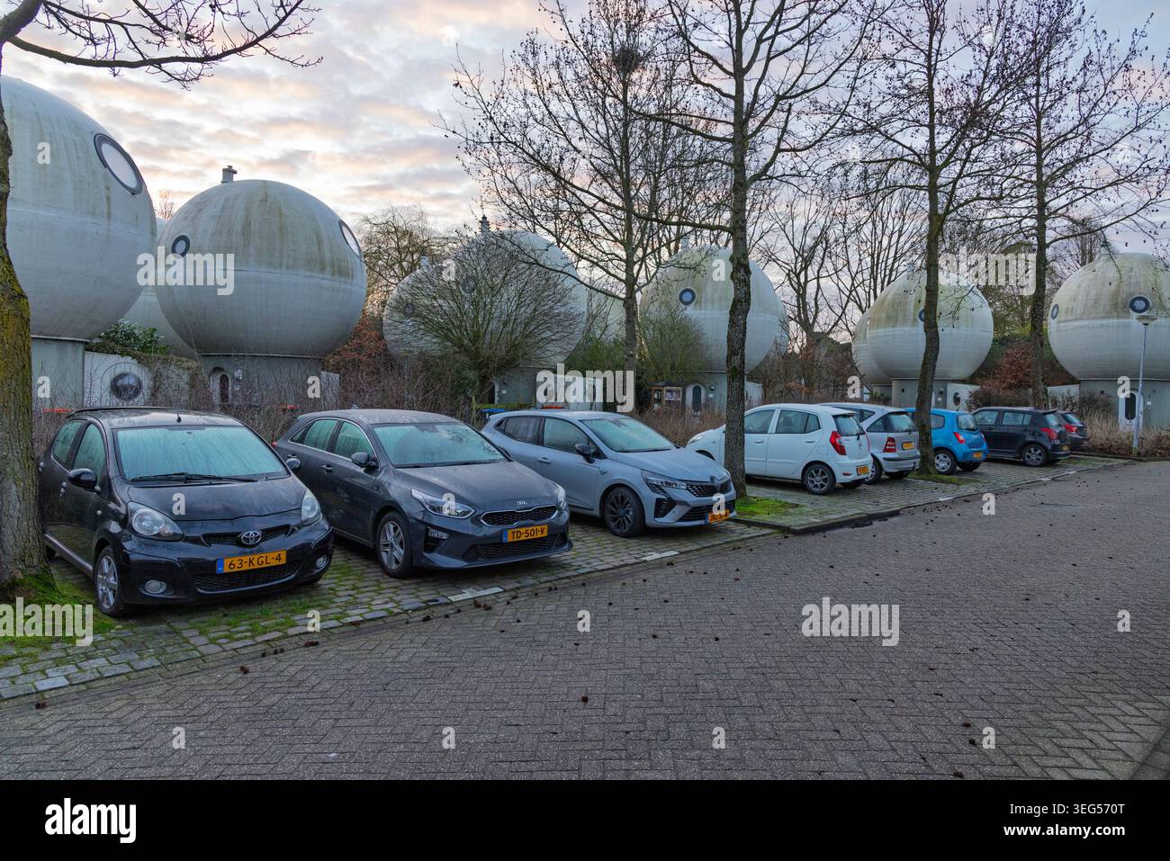 Den Bosch, Paesi Bassi - 01 marzo 2026 - fila di auto moderne parcheggiate lungo la strada di fronte all'innovativo quartiere sferico di Bolwoningen. Foto Stock