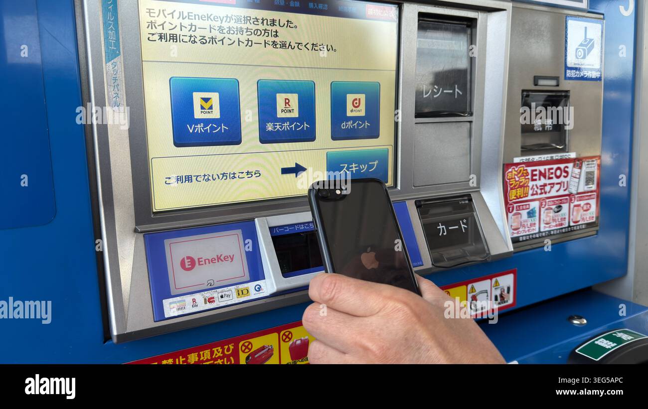 Un cliente ha uno smartphone davanti a un touchscreen self-service per erogatori di carburante mentre sceglie un programma fedeltà presso una stazione ENEOS EneJet. Foto Stock