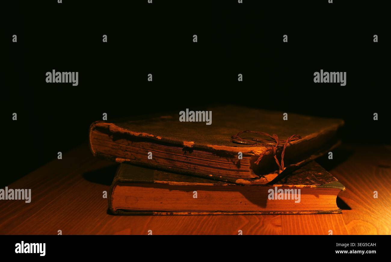 Due libri vintage rilegati in pelle poggiati su un caldo tavolo in legno, illuminati da una luce morbida e direzionale che crea un'atmosfera misteriosa e storica Foto Stock