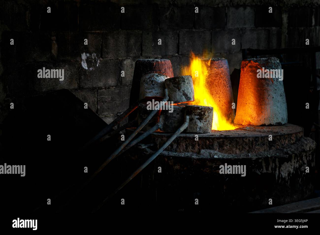 Crogioli industriali riscaldati dal fuoco intenso all'interno di un'officina buia durante i processi di produzione della fusione dei metalli. Foto Stock