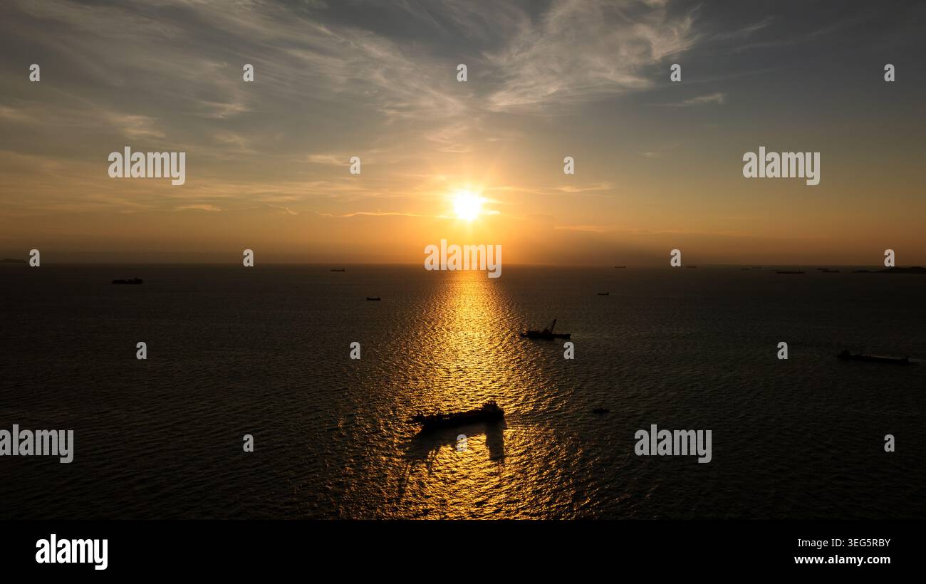 Le navi da carico si stagliavano contro un tramonto vibrante sull'oceano che rappresentava la spedizione e la logistica globale. Foto Stock