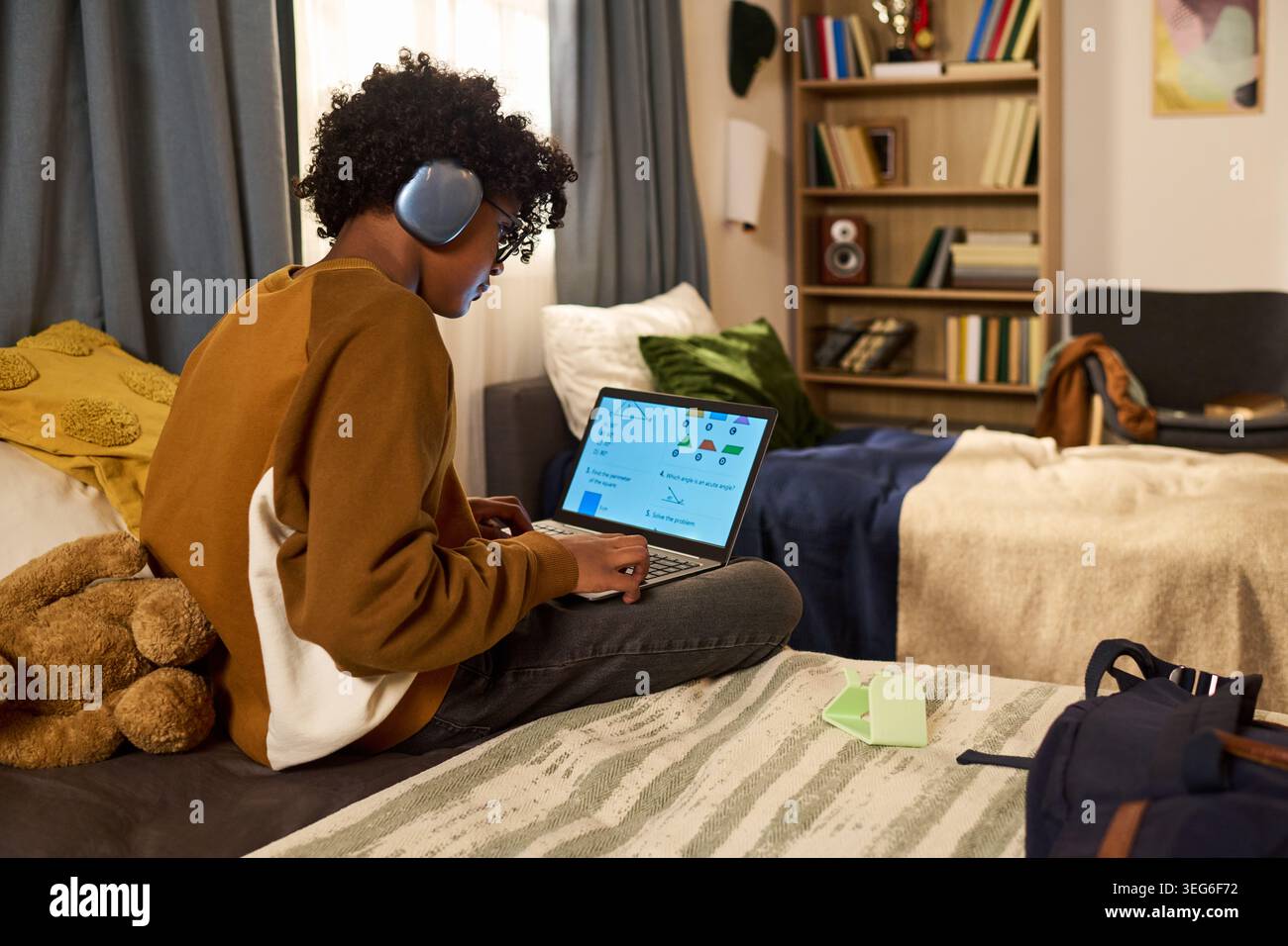 Adolescente che indossa le cuffie e usa il laptop per imparare online in camera da letto, studiare geometria e concetto di educazione remota. Vista laterale per l'edtech, il marketing per la homeschooling Foto Stock