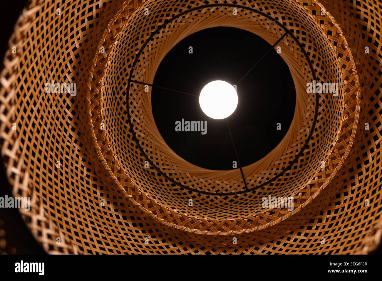 Vista dal basso della lampadina a incandescenza all'interno del paralume di bambù in vimini motivo geometrico Foto Stock