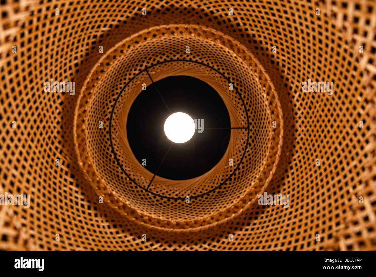 Vista dal basso della lampadina a incandescenza all'interno del paralume di bambù in vimini motivo geometrico Foto Stock