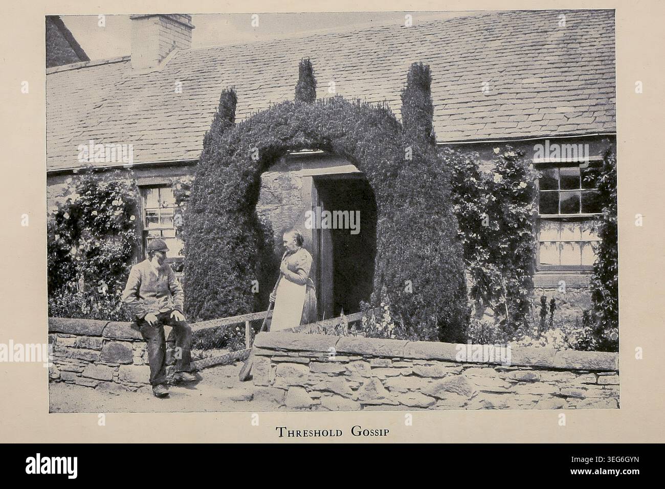 Due abitanti del villaggio, un uomo seduto su un muro di pietra e una donna in piedi su una porta incorniciata da un lussureggiante arco di siepe, impegnati in una conversazione fuori dalla loro tradizionale casa rurale. Da ' The Land of heather' di Clifton Johnson, 1865-1940 data di pubblicazione 1903 Foto Stock