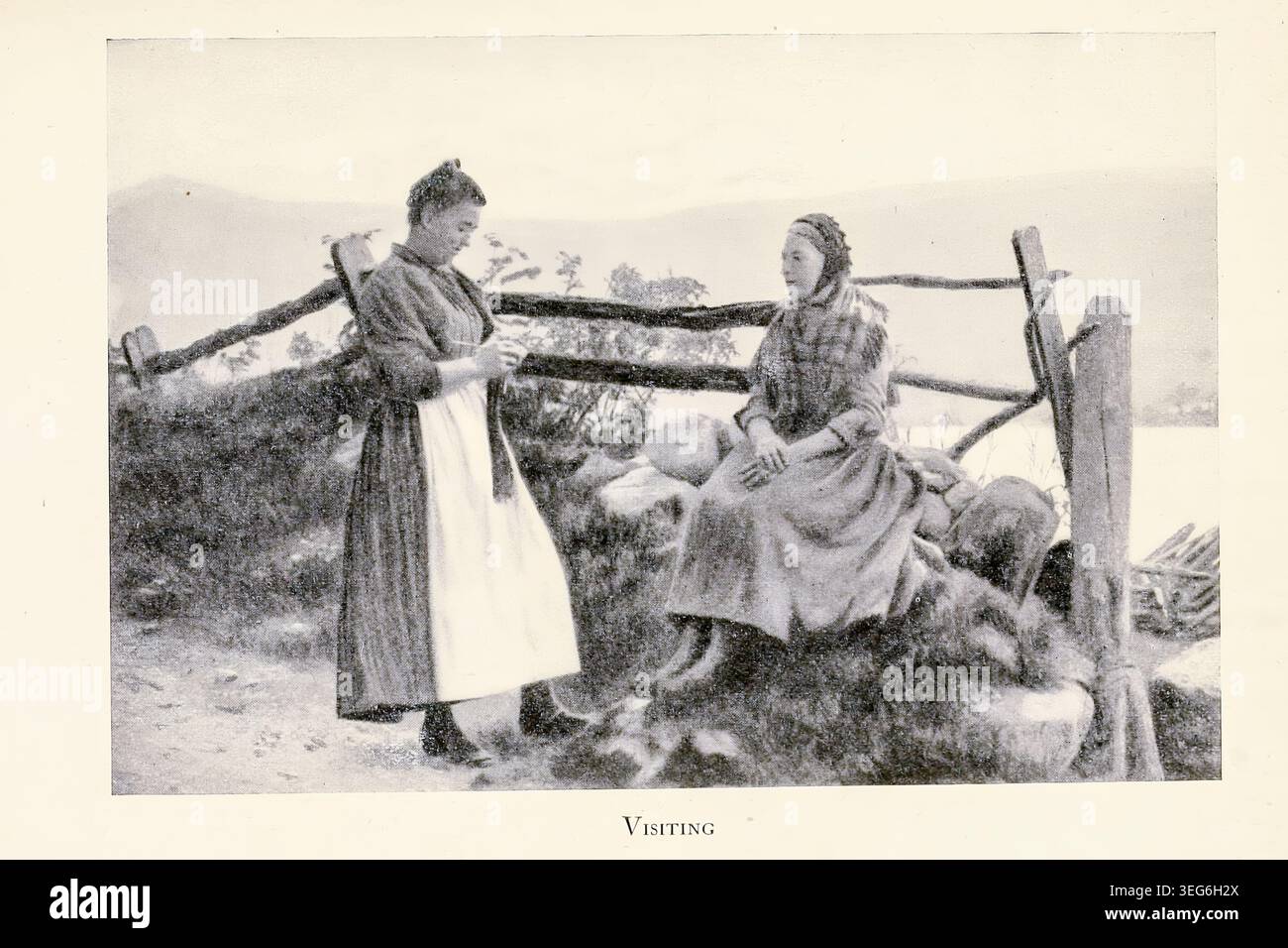 Due donne rurali in tradizionali cofani e scialli condividono una tranquilla visita presso un muro di pietra, un filato a maglia mentre conversano contro una recinzione serena e un paesaggio lontano. Da ' The Land of heather' di Clifton Johnson, 1865-1940 data di pubblicazione 1903 Foto Stock