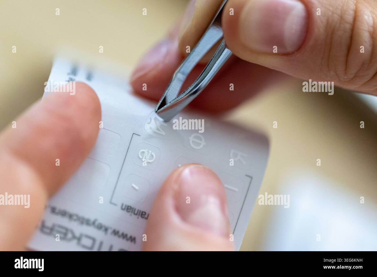 Mani che prendono e applicano adesivi con pinzette sulla tastiera inglese, caratteri alfabetici cirillici per la digitazione multilingue Foto Stock