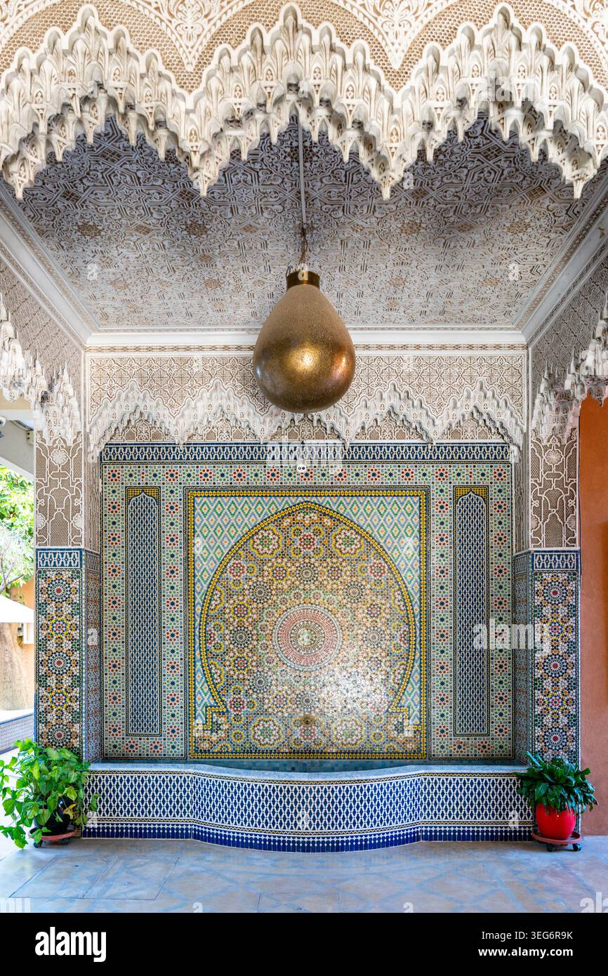 Fontana decorata a mosaico marocchino sotto un soffitto intagliato a Marrakech Foto Stock