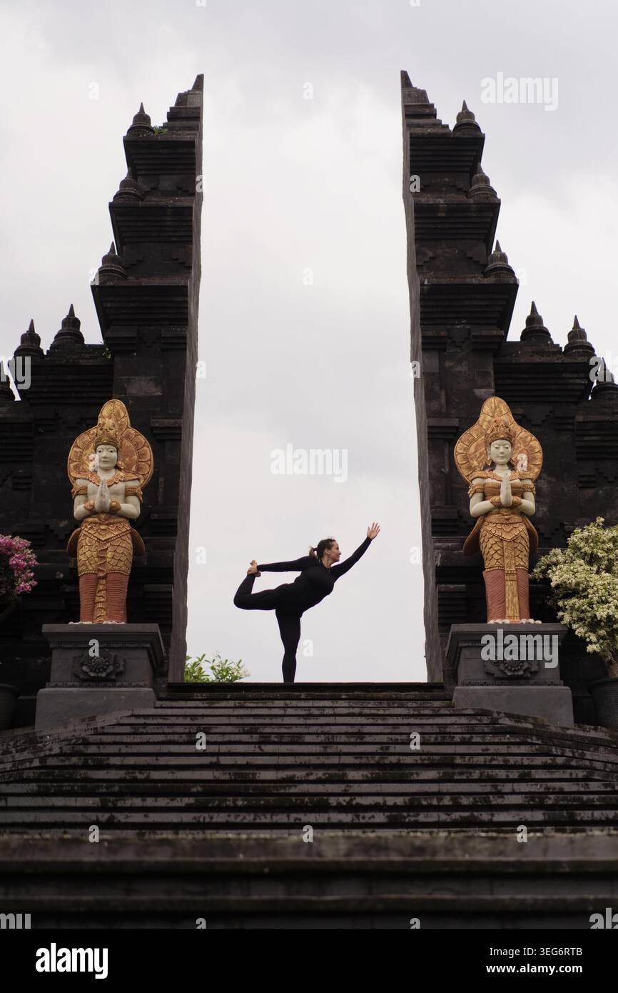 Una donna ballerina posa yoga al cancello del tempio balinese con statue, Bali Foto Stock