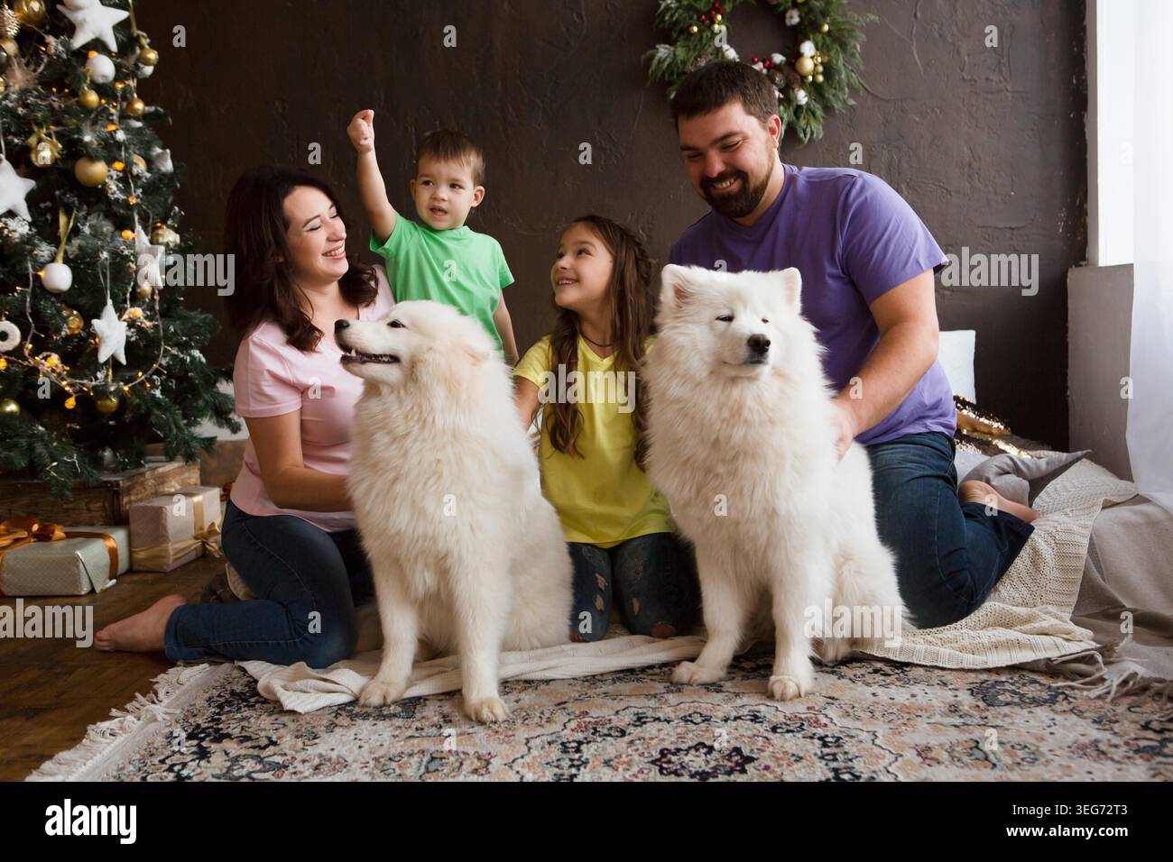 Famiglia felice con il cane samoyed husky seduto vicino al bellissimo albero di Natale a casa. Foto Stock