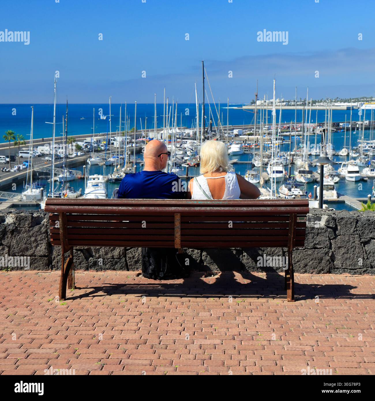 Coppia di mezza età seduta su una panchina con vista su Marina Rubicon, Playa Blanca, Lanzarote, Isole Canarie, Spagna, Europa Foto Stock