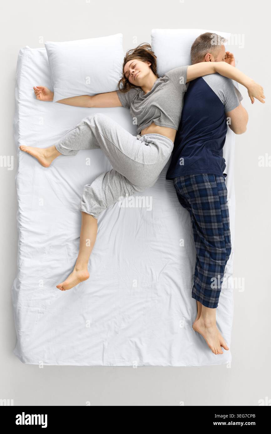 Donna che si allunga sul letto bianco mentre l'uomo dorme schiena a schiena. Foto Stock