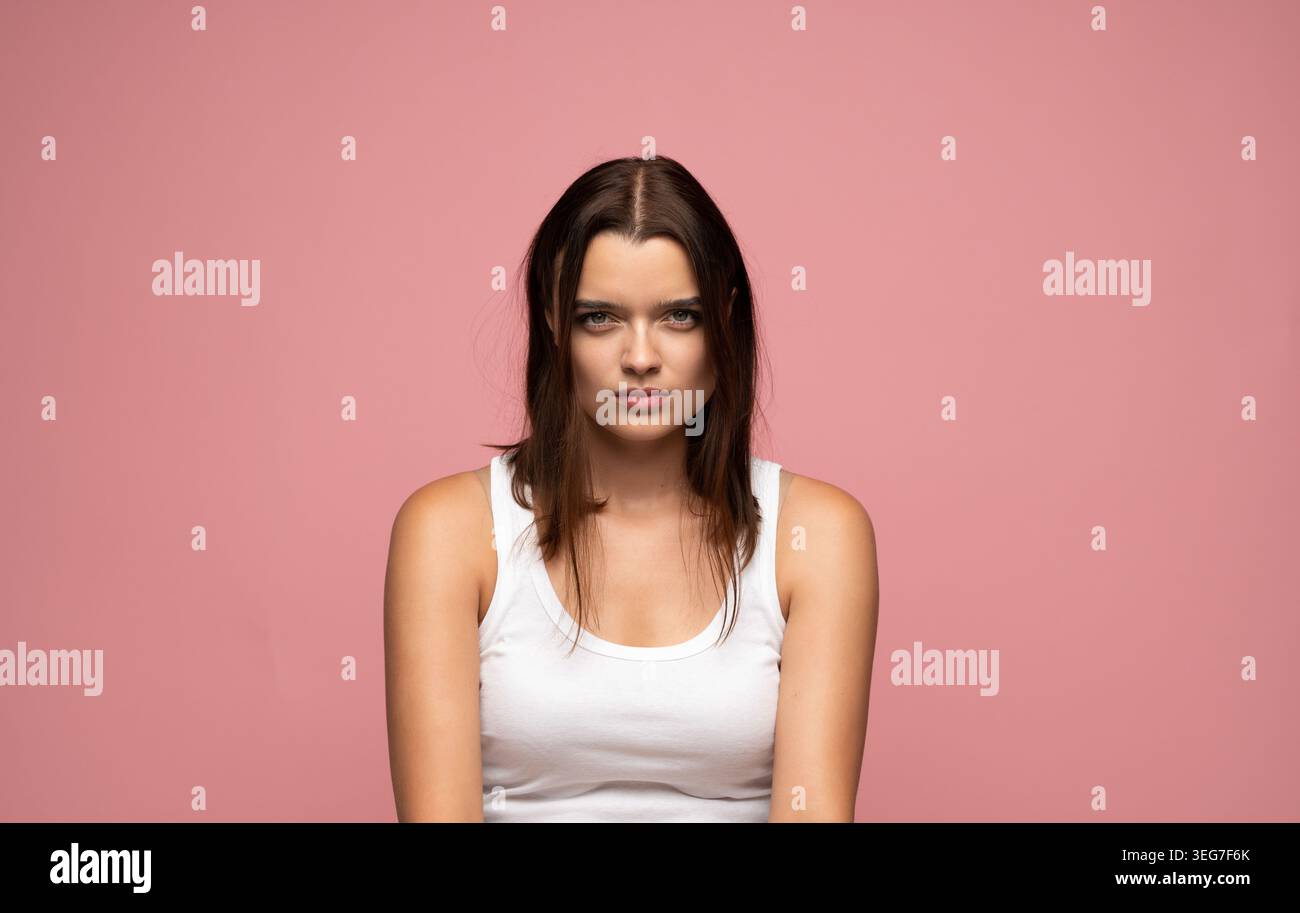 Giovane donna con un'espressione intensa e uno sguardo diretto rivolto verso la fotocamera su sfondo rosa Foto Stock