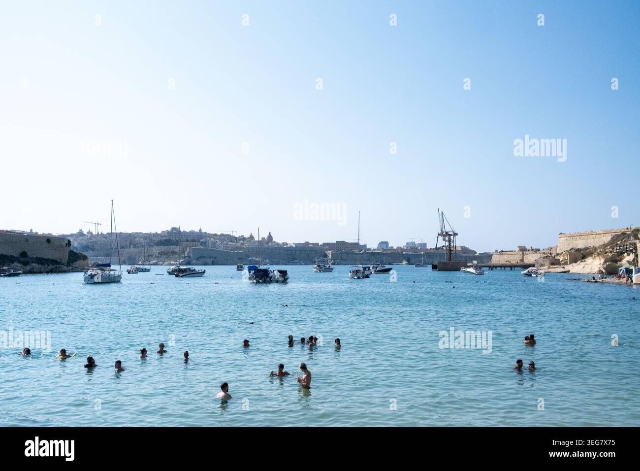 Vista dei nuotatori in acqua a Rinella Bay con barche, riva calcarea e fronte mare a Kalkara, regione sud-orientale, Malta, 9 agosto Foto Stock