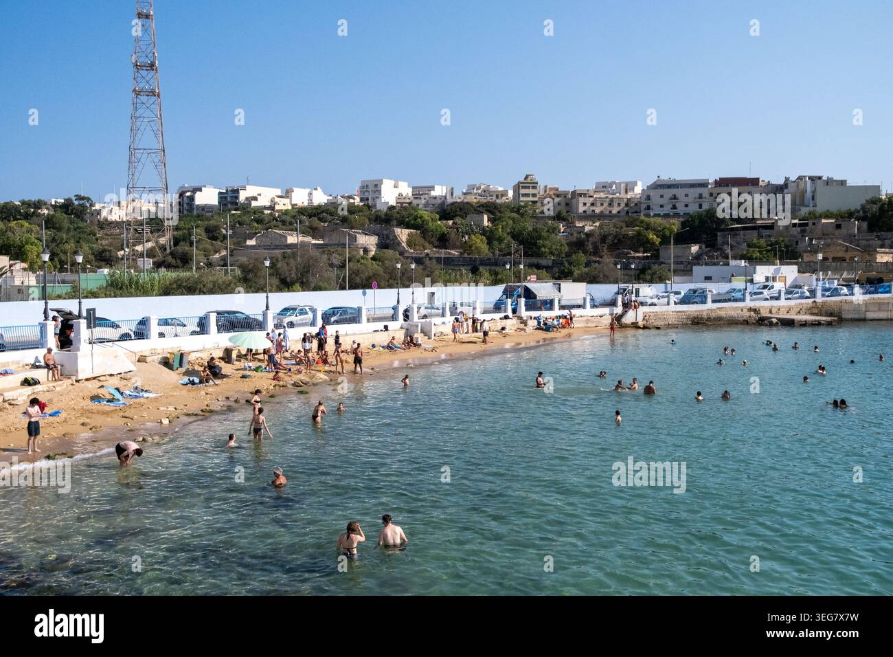 Vista dei bagnanti e dei bagnanti della baia di Rinella con nuotatori nel mare, una spiaggia sabbiosa e il lungomare di Kalkara, regione sud-orientale, Malta, Augu Foto Stock