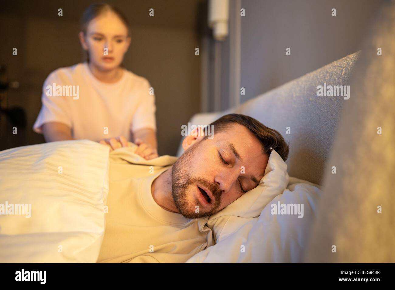 Donna frustrata che cerca di impedire al marito di russare di notte, spingendo l'uomo sulla spalla per svegliarsi. Foto Stock