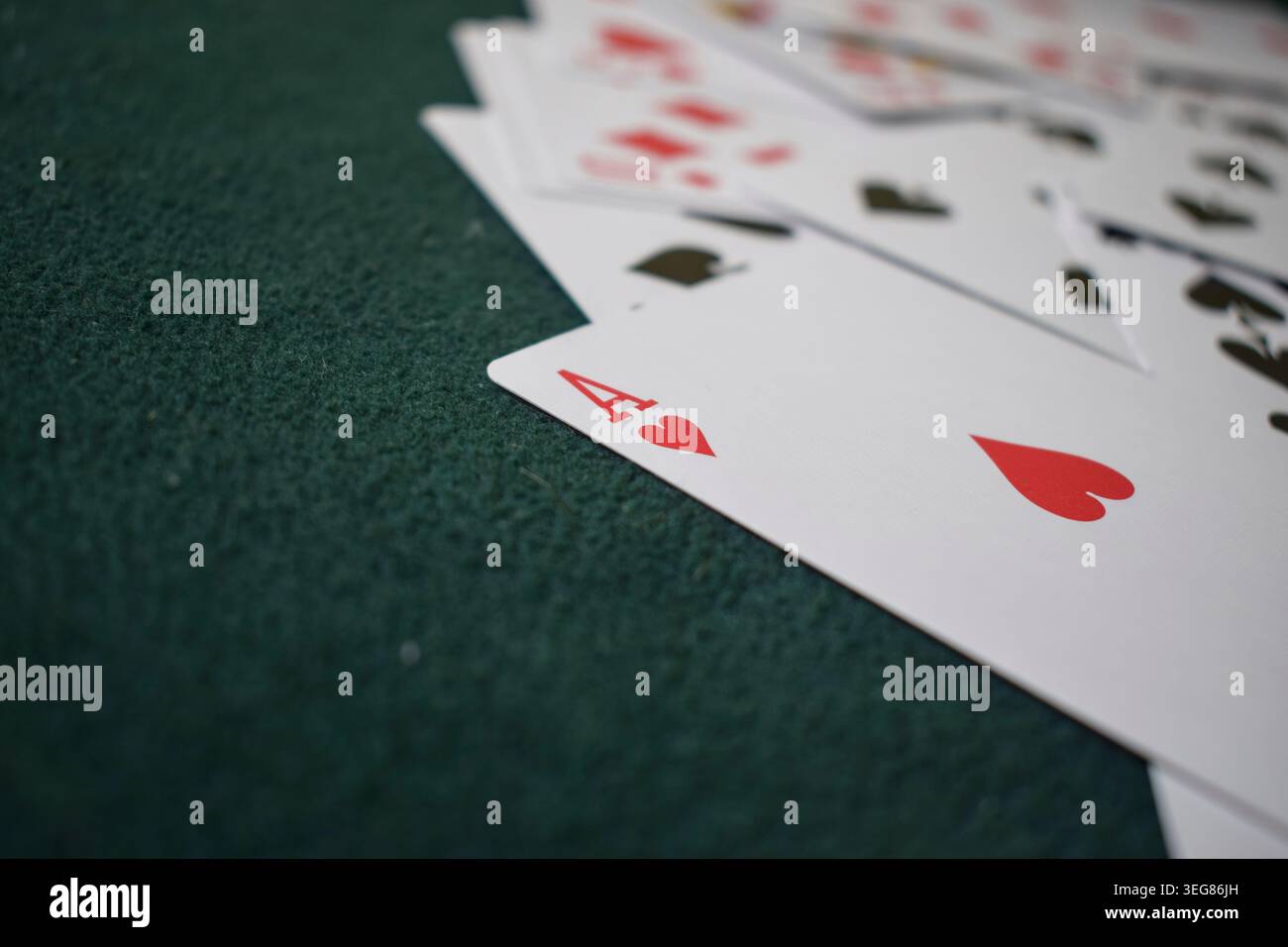Una carta da gioco Ace of Hearts poggiata su un tavolo da poker in feltro verde con altre carte. Foto Stock