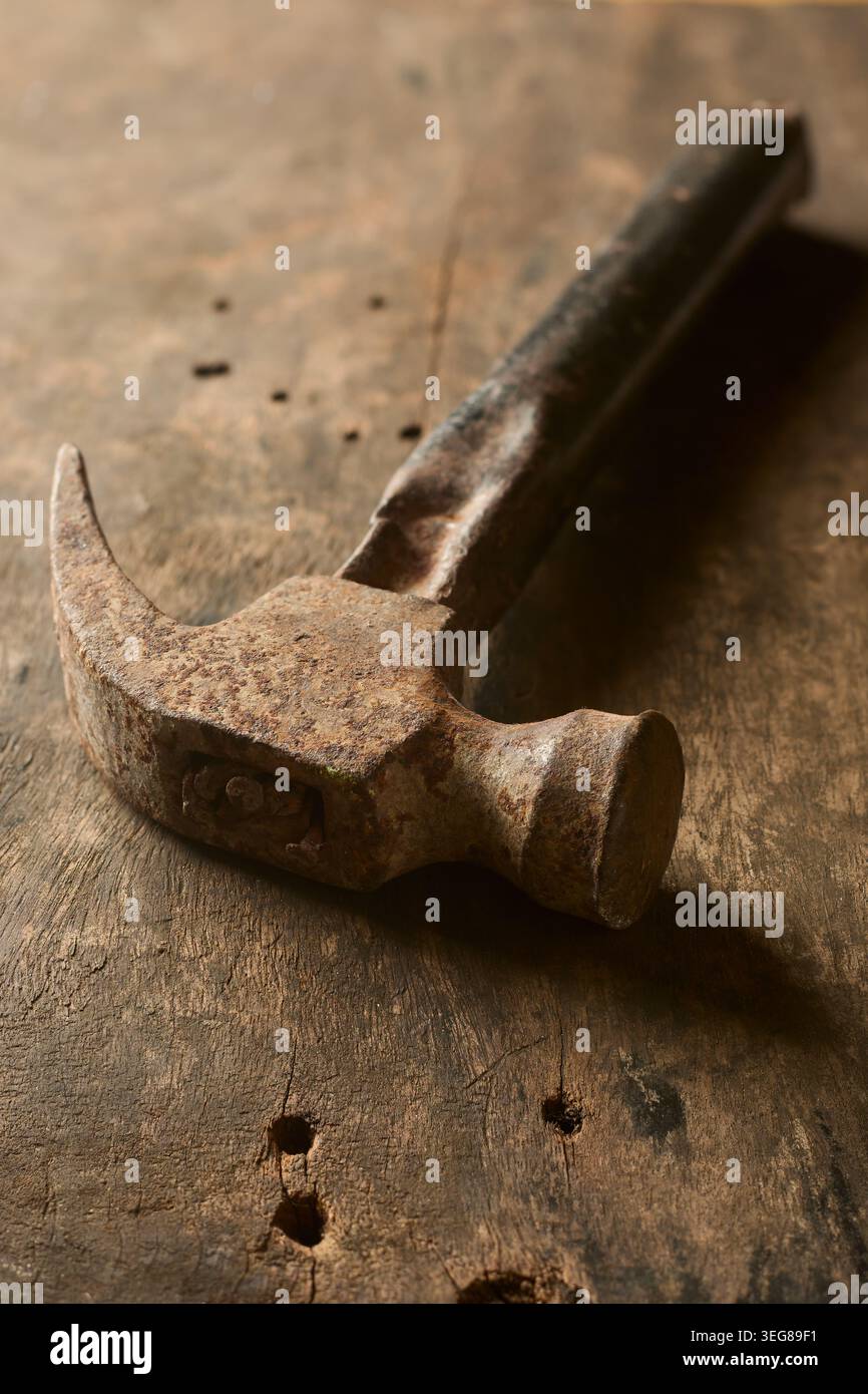 martello a baionetta in ferro arrugginito d'epoca con impugnatura scura usurata sulla superficie del banco da lavoro in legno, primo piano con messa a fuoco morbida e spazio di copia Foto Stock