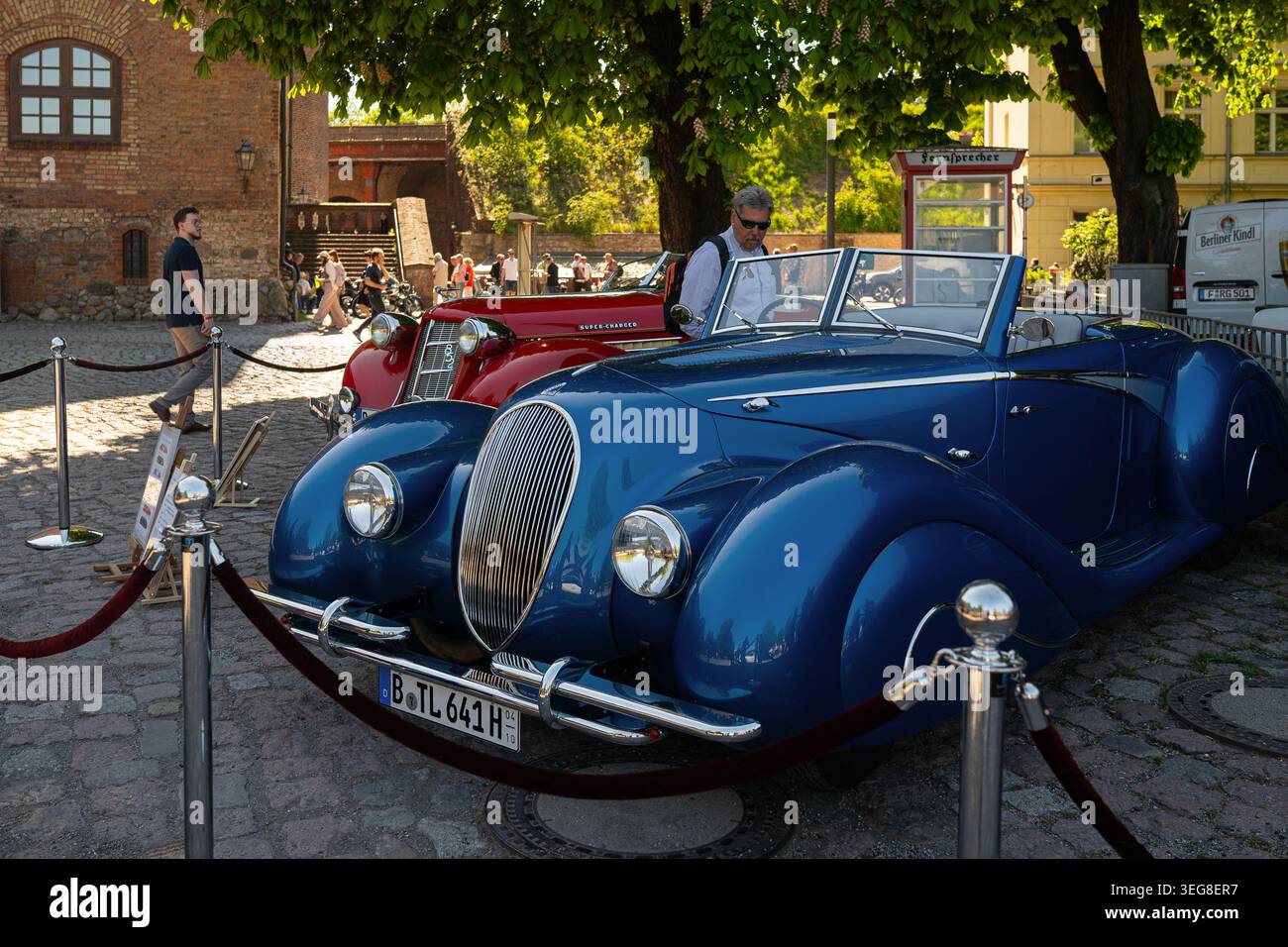 Berlino, Germania - 2 maggio 2026. Roadster d'epoca blu e rosso esposti dietro una barriera di corda in una mostra di auto d'epoca all'aperto vicino agli edifici storici A. Foto Stock